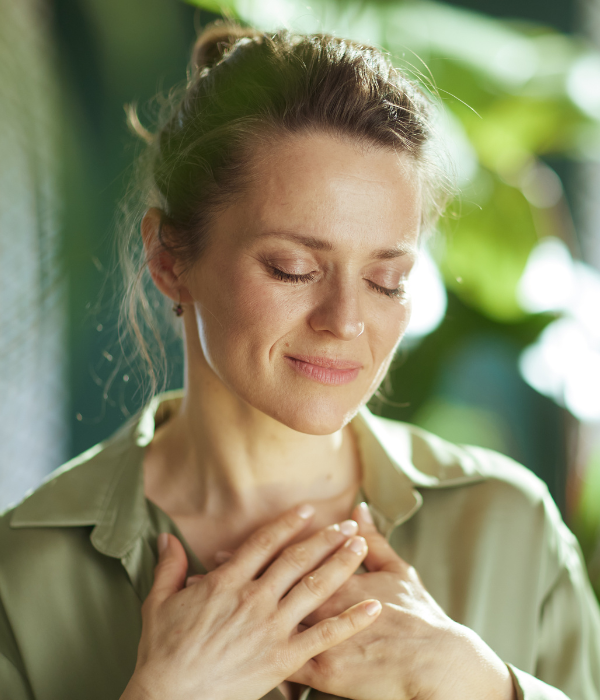 A woman holding her hands to her heart and closing her eyes with a soft smile to depict moving forward with a better relationship with herself, thanks to the help of online counseling at Palmetto Counseling.